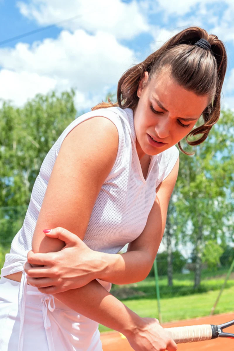 Teniszező nő könyökfájdalmat érez a teniszpályán, a teniszkönyök tüneteivel.