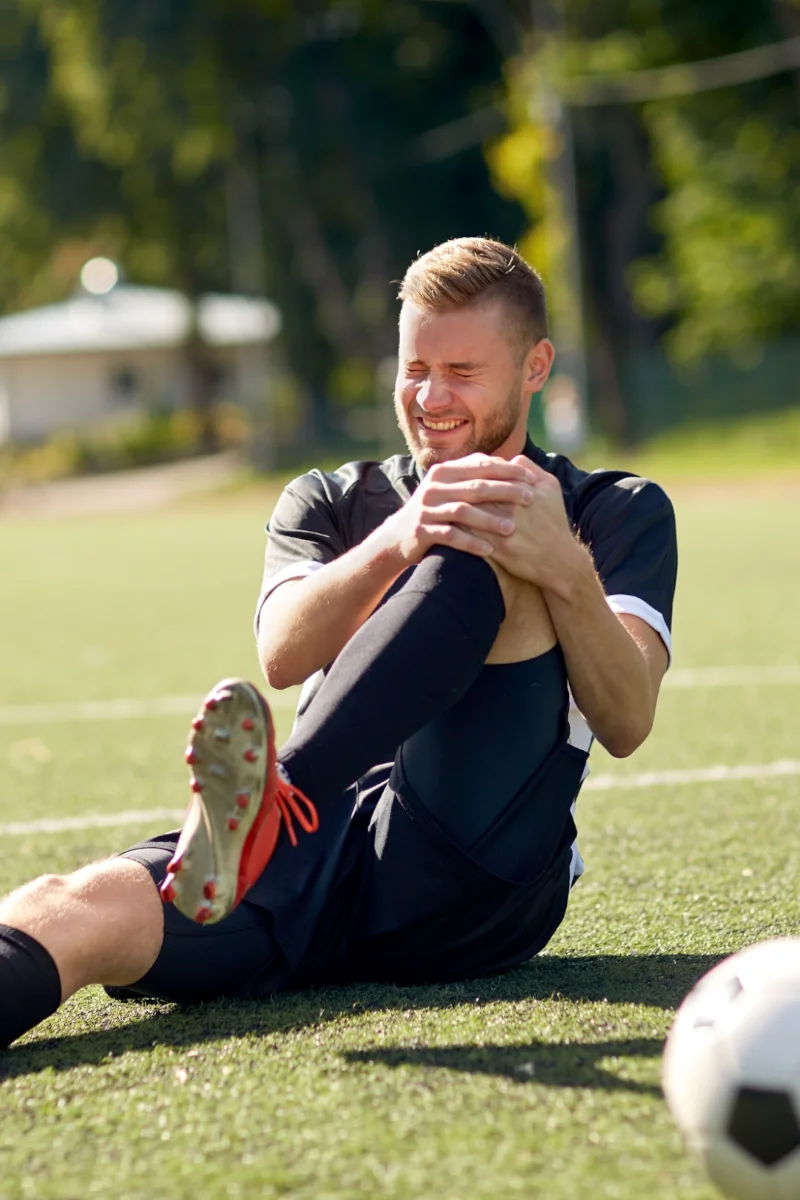 Sportolás közbeni porc sérülés miatt földön ülő focista. Porchiány a térdben fiataloknál, porcpótlás a térdben sportolók számára.